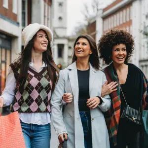 Three cheerful female friends enjoy a shopping spree, carrying bags and strolling down a bustling city street