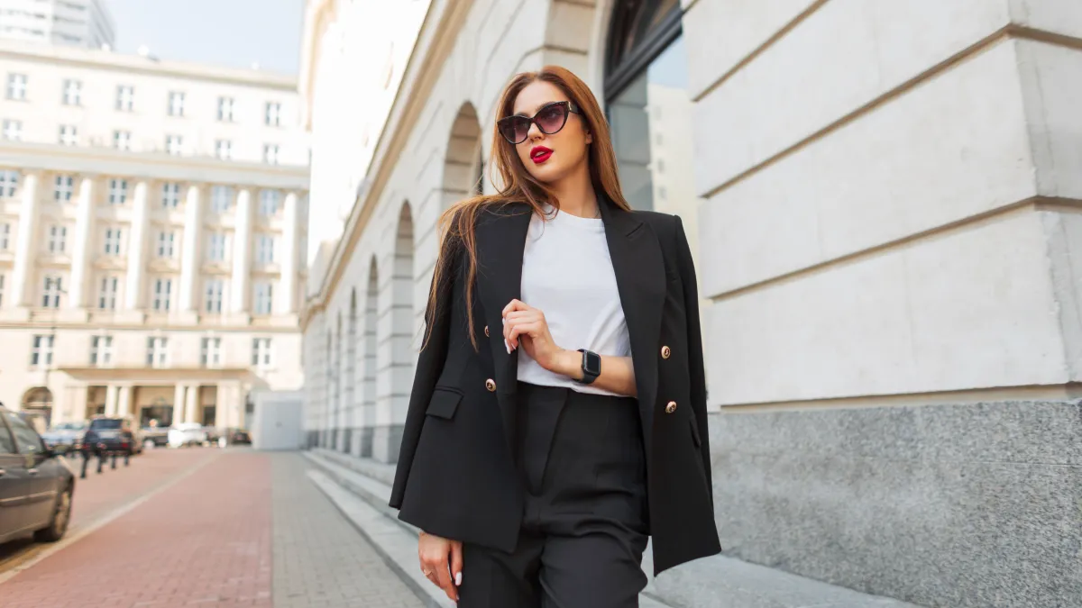 Beautiful urban fashion woman in a stylish black casual suit with vintage sunglasses walks in the city. Pretty business lady