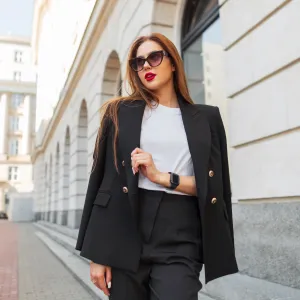 Beautiful urban fashion woman in a stylish black casual suit with vintage sunglasses walks in the city. Pretty business lady