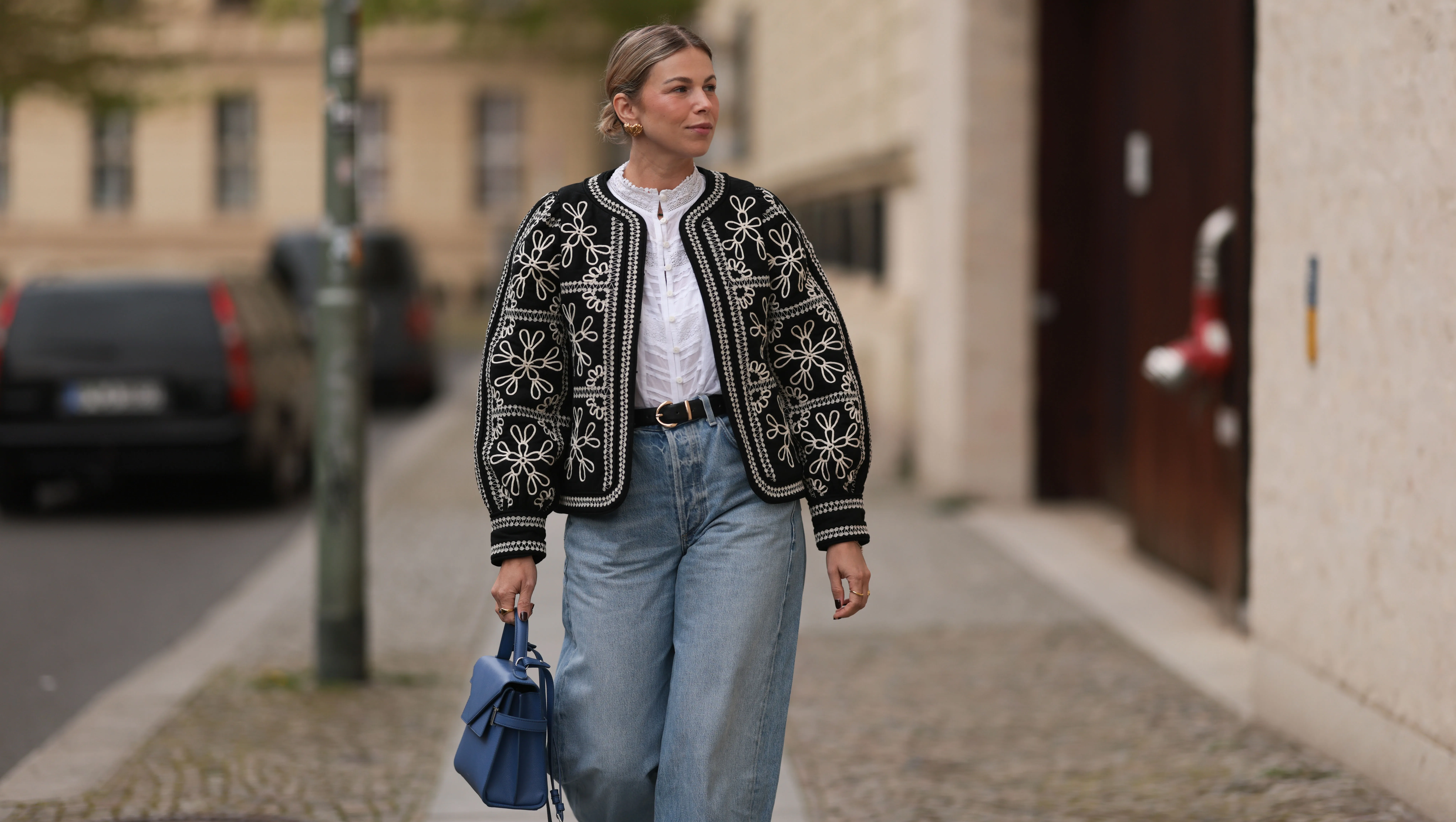 BERLIN, GERMANY - APRIL 08: Aline Kaplan seen wearing gold heart shaped earrings, Sézane black / white flower embroidered jacket, Mango white cotton blouse, Citizen Of Humanity blue denim wide leg jeans, Le Tanneur blue leather bag, on April 08, 2024 in Berlin, Germany.