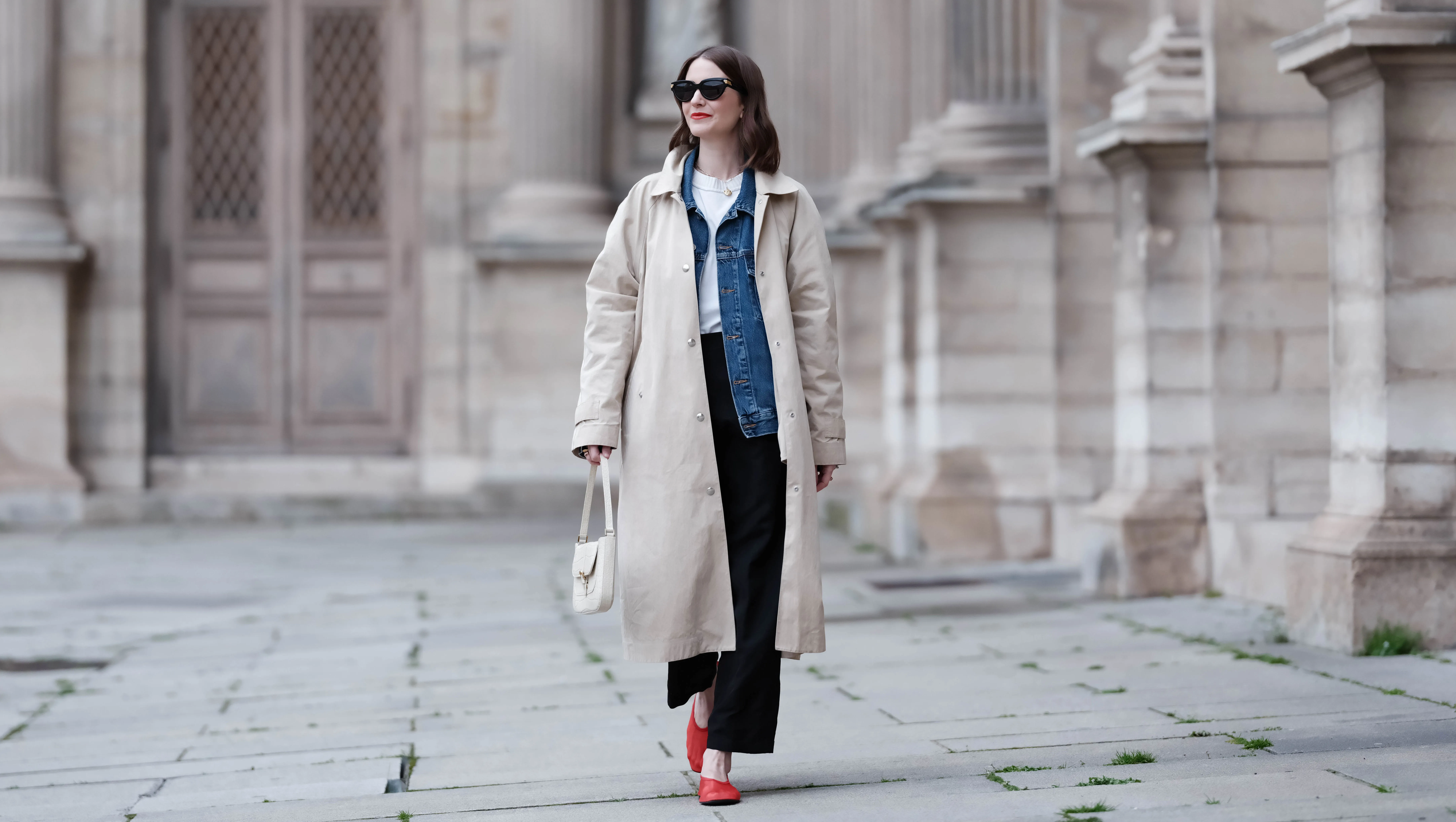 Marissa Cox wears Massimo Dutti black trousers, Agolde white t-shirt and blue denim jacket, Arket car coat and red mesh flats, By Far cream bag and Bottega Vanetta sunglasses, during a street style fashion photo session, on March 30, 2024 in Paris, France.
