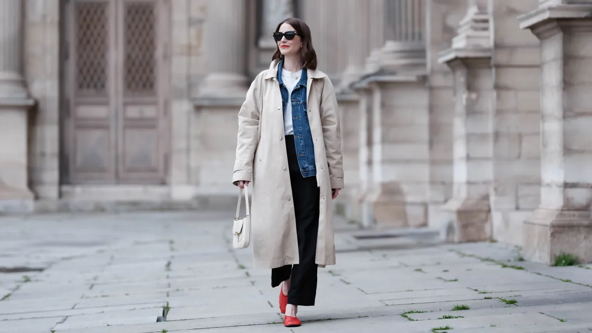 Marissa Cox wears Massimo Dutti black trousers, Agolde white t-shirt and blue denim jacket, Arket car coat and red mesh flats, By Far cream bag and Bottega Vanetta sunglasses, during a street style fashion photo session, on March 30, 2024 in Paris, France.