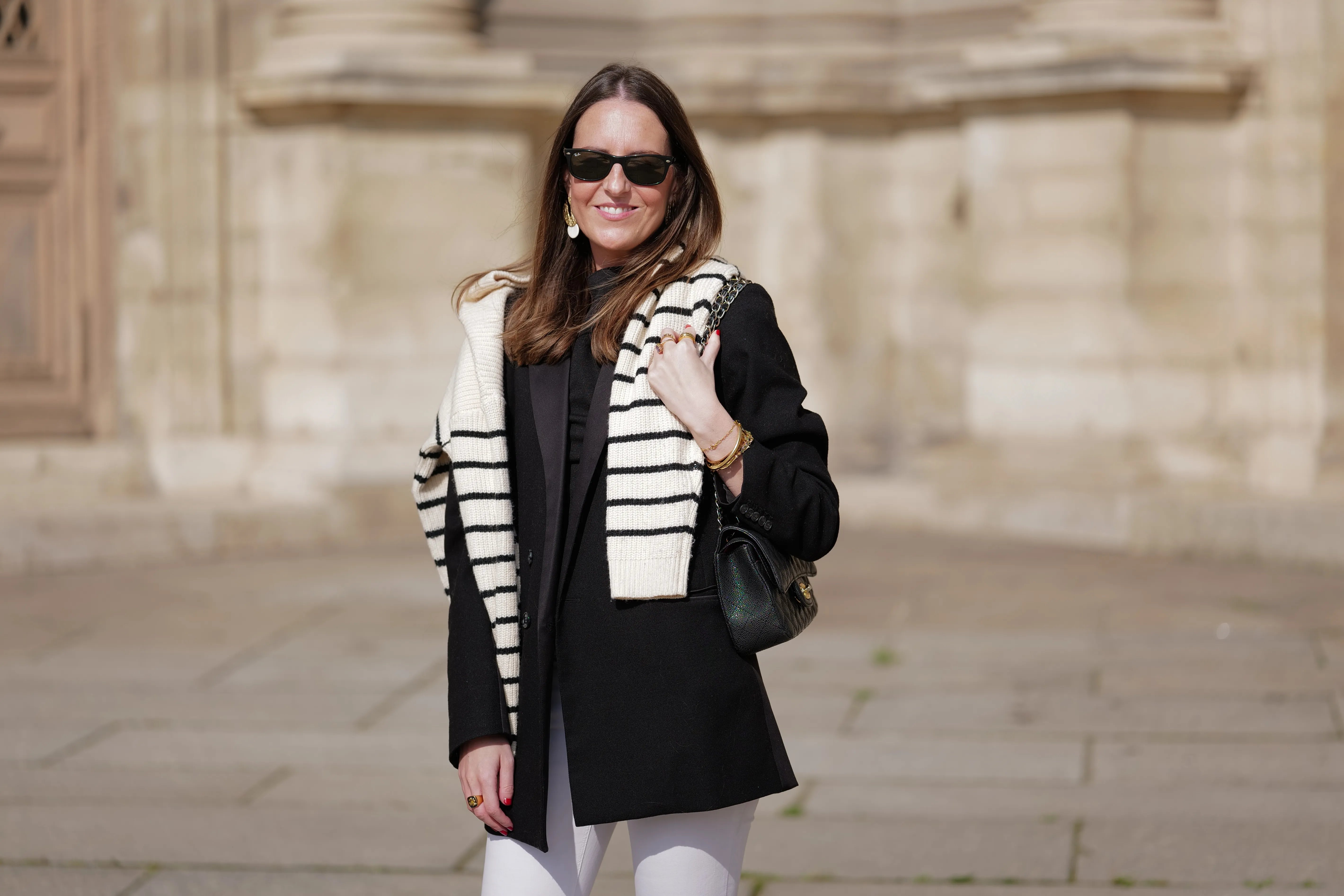 woman wearing black coat, striped sweater and white pants