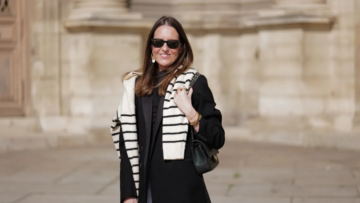 woman wearing black coat, striped sweater and white pants