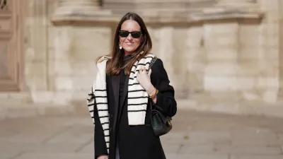 woman wearing black coat, striped sweater and white pants
