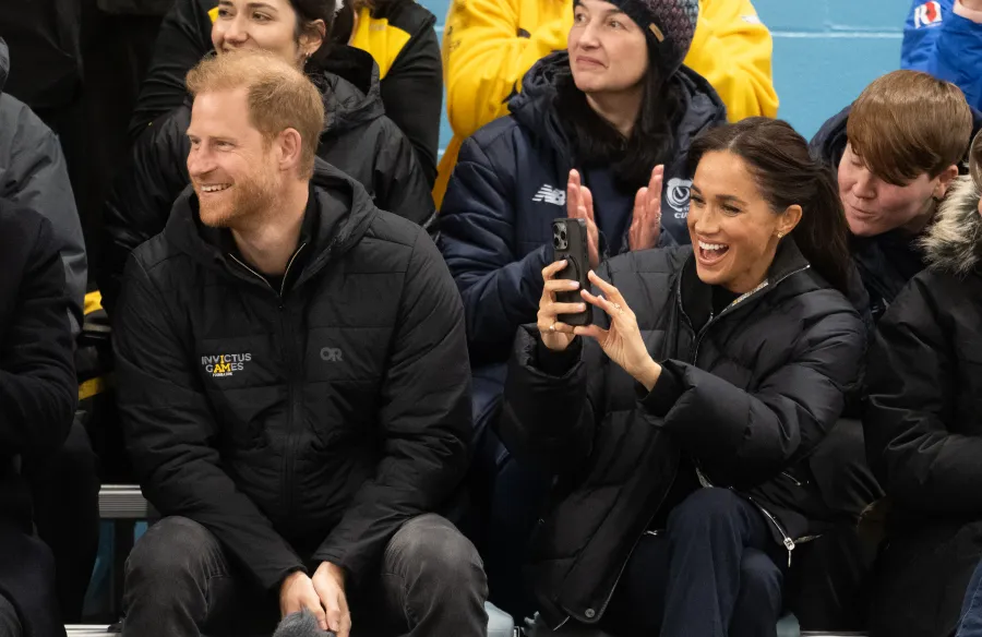 Meghan Markle takes a photo on her phone while Prince Harry smiles