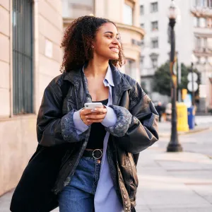 Portrait with motion and copy space of a smiley afro woman using a mobile walking in the street