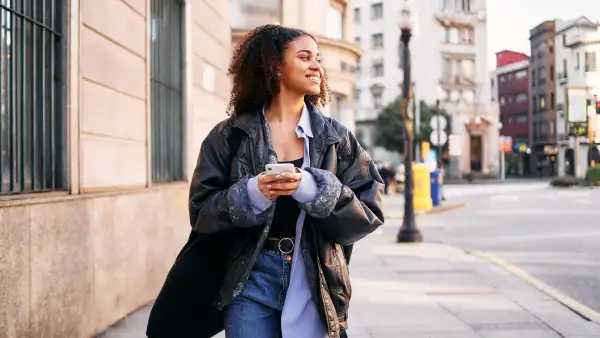 Portrait with motion and copy space of a smiley afro woman using a mobile walking in the street