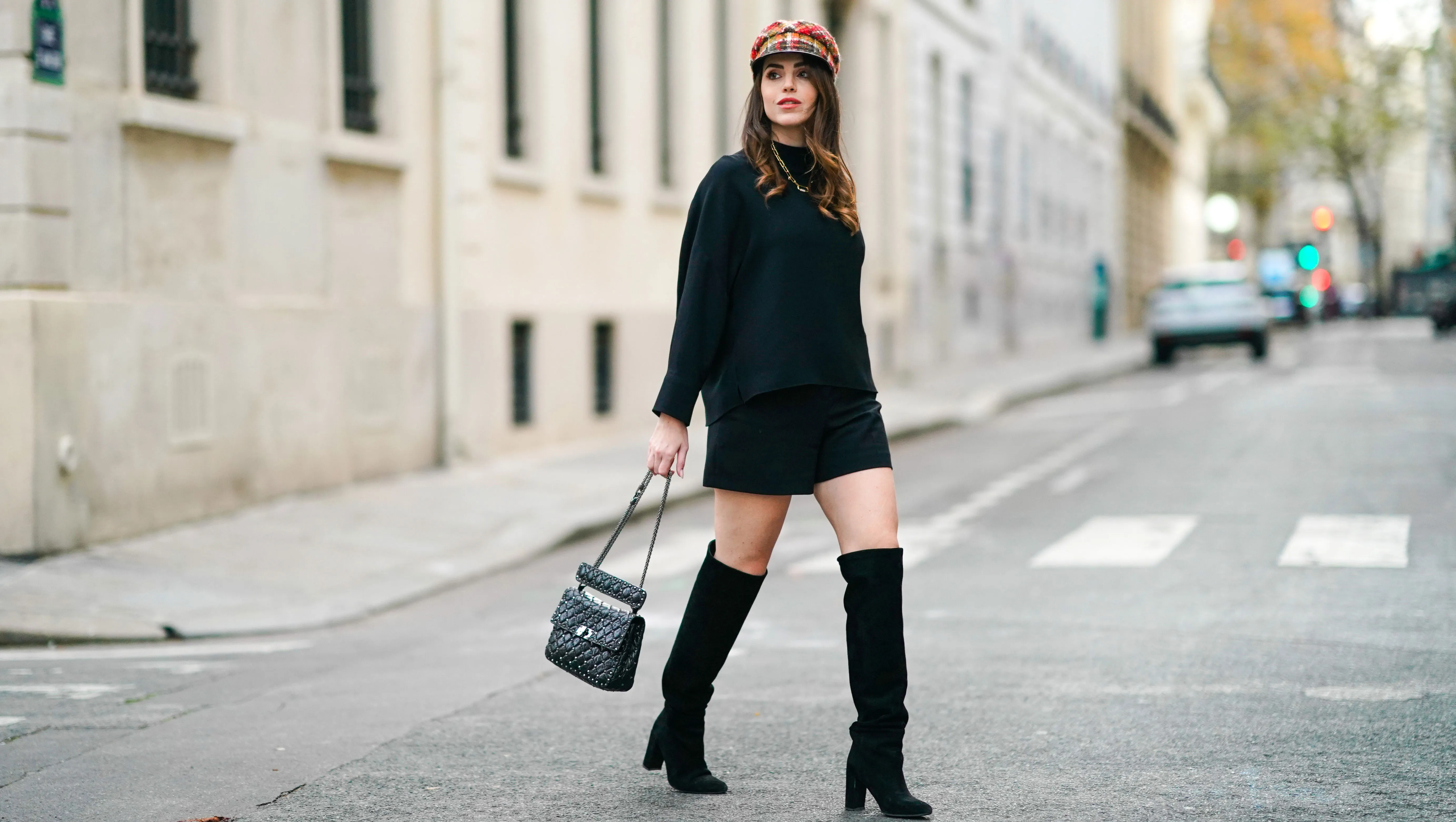 PARIS, FRANCE - NOVEMBER 14: Sara Carnicella wears a red checked beret hat from Anthony Peto, a black oversized pullover from Natan, a black leather studded Valentino Rockstud bag, Zara black shorts, black pointy knee-high boots from Jonak, a golden necklace from APM Monaco, on November 14, 2020 in Paris, France.