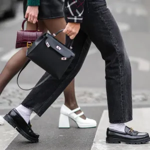 PARIS, FRANCE - MARCH 02: A guest wears a black with white and red checkered print pattern jacket, black faded denim large jeans pants, white socks, a black shiny leather Kelly handbag from Hermes, black shiny leather with gold logo buckle loafers from Celine , outside Courreges, during Paris Fashion Week - Womenswear F/W 2022-2023, on March 02, 2022 in Paris, France.