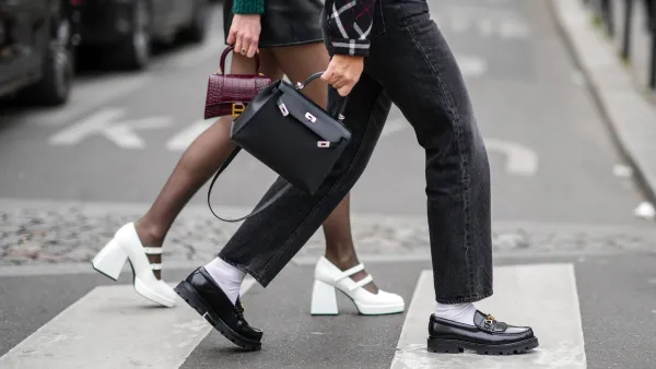 PARIS, FRANCE - MARCH 02: A guest wears a black with white and red checkered print pattern jacket, black faded denim large jeans pants, white socks, a black shiny leather Kelly handbag from Hermes, black shiny leather with gold logo buckle loafers from Celine , outside Courreges, during Paris Fashion Week - Womenswear F/W 2022-2023, on March 02, 2022 in Paris, France.