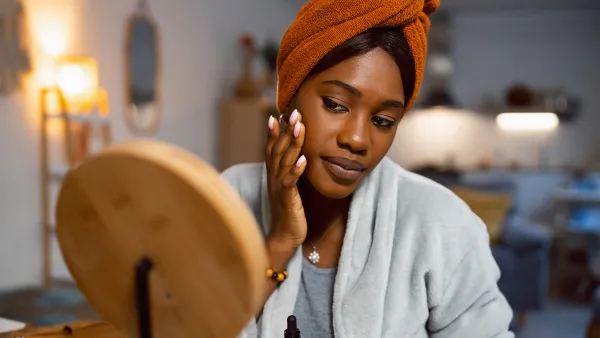 Young woman of Black ethnicity, applying a face serum, while doing a skin care routine