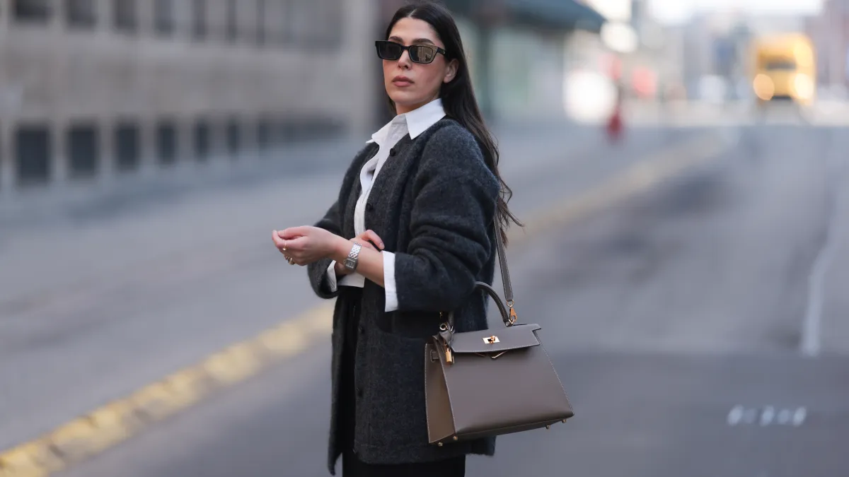 HAMBURG, GERMANY - MARCH 08: Tugba Kement seen wearing black sunglasses, Sézane dark grey wool knit long cardigan, white cotton buttoned shirt, COS black midi long skirt, Hermès Kelly taupe / brown leather bag, gold rings and Cartier Panthère bicolor watch, on March 08, 2024 in Hamburg, Germany. (Photo by Jeremy Moeller/Getty Images)