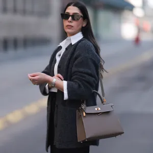 HAMBURG, GERMANY - MARCH 08: Tugba Kement seen wearing black sunglasses, Sézane dark grey wool knit long cardigan, white cotton buttoned shirt, COS black midi long skirt, Hermès Kelly taupe / brown leather bag, gold rings and Cartier Panthère bicolor watch, on March 08, 2024 in Hamburg, Germany. (Photo by Jeremy Moeller/Getty Images)