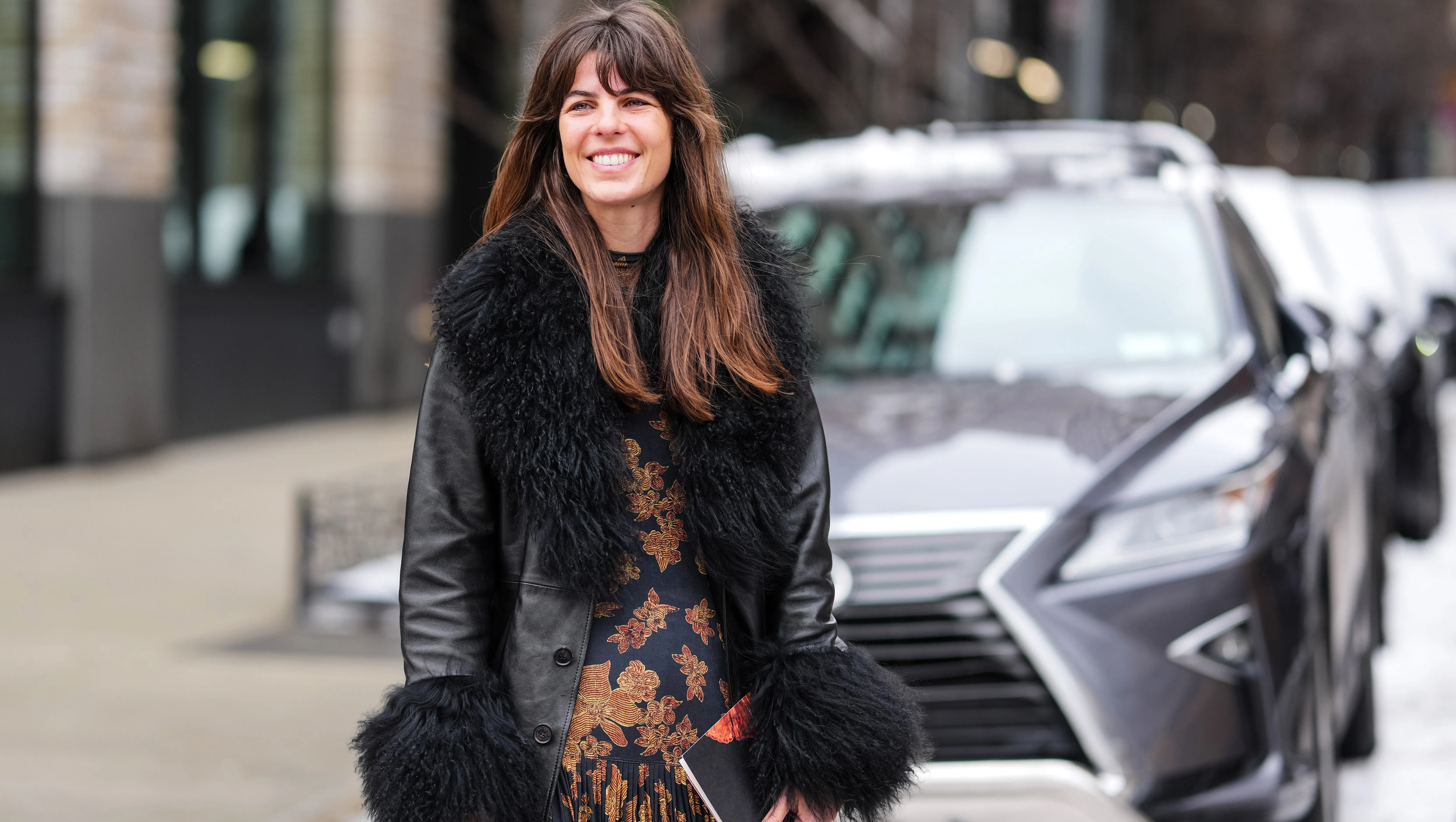 NEW YORK, NEW YORK - FEBRUARY 09: A guest wears shiny black faux fur collar cuff leather coat, black gold floral pattern maxi dress, outside Ulla Johnson, during the New York Fashion week Fall/Winter 2025 on February 9, 2025 in New York, New York. (Photo by Edward Berthelot/Getty Images)
