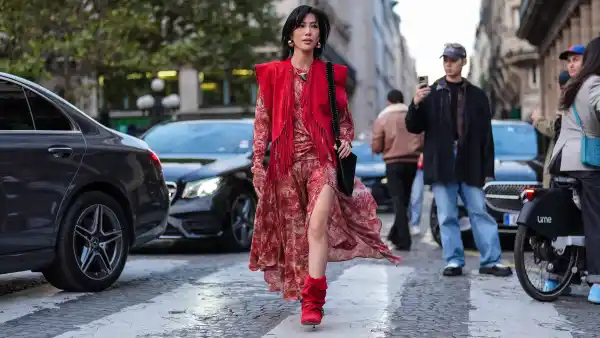 PARIS, FRANCE - SEPTEMBER 29: Molly Chiang wears gold earrings, bright red tassel vest, dark red floral pattern/print long sleeve flowy midi dress, silver pendant necklace, bright red suede slouchy kitten heel Isabel Marant boots, black bag, outside Isabel Marant, during the Paris Fashion week Spring/Summer 2025 on September 29, 2024 in Paris, France (Photo by Edward Berthelot/Getty Images)