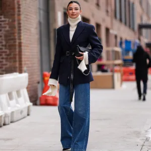 NEW YORK, NEW YORK - FEBRUARY 11: Kelsey Merritt wears cream turtleneck Michael Kors sweater, dark navy blue Michael Kors blazer jacket, shiny black Michael Kors leather belt, shiny black Michael Kors leather bag, navy blue wide leg denim jean pants, outside Michael Kors, during the New York Fashion week Fall/Winter 2025 on February 11, 2025 in New York, New York. (Photo by Edward Berthelot/Getty Images)