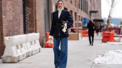 NEW YORK, NEW YORK - FEBRUARY 11: Kelsey Merritt wears cream turtleneck Michael Kors sweater, dark navy blue Michael Kors blazer jacket, shiny black Michael Kors leather belt, shiny black Michael Kors leather bag, navy blue wide leg denim jean pants, outside Michael Kors, during the New York Fashion week Fall/Winter 2025 on February 11, 2025 in New York, New York. (Photo by Edward Berthelot/Getty Images)