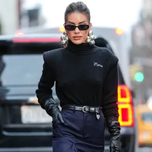 NEW YORK, NEW YORK - FEBRUARY 09: Camila Coelho wears black sunglasses, silver earrings, black turtle long sleeve sweater, shiny black leather gloves, shiny black leather belt, black high waisted high slit midi skirt, shiny black pointed toe knee high leather boots, shiny black alaïa leather bag, outside Monse, during the New York Fashion week Fall/Winter 2025 on February 9, 2025 in New York, New York. (Photo by Edward Berthelot/Getty Images)