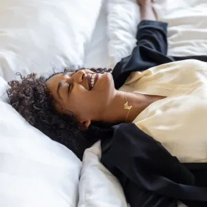 Tired mid adult businesswoman lying on hotel bed after her trip. Tired woman in formal clothes resting on hotel bed with her arms outstretched and smiling.