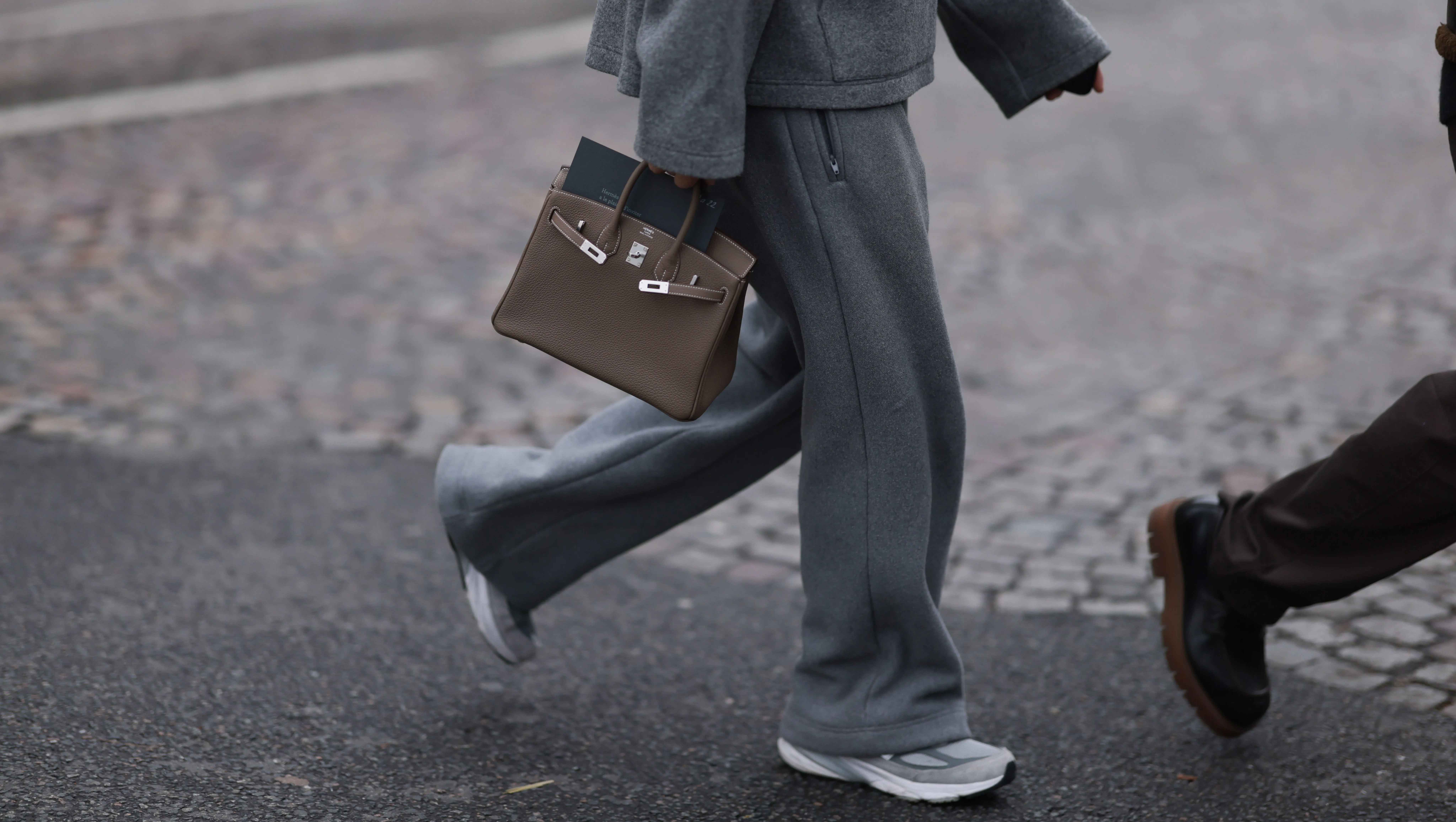PARIS, FRANCE - JANUARY 25: Fashion Week Guest seen wearing a grey jogging suit, jacket, wide jogging pants and sport sneaker, Hermes taupe Birkin bag outside Hermes Show, during the Menswear Fall Winter 2025/2026 as part of Paris Fashion Week on January 25, 2025 in Paris, France. (Photo by Jeremy Moeller/Getty Images)