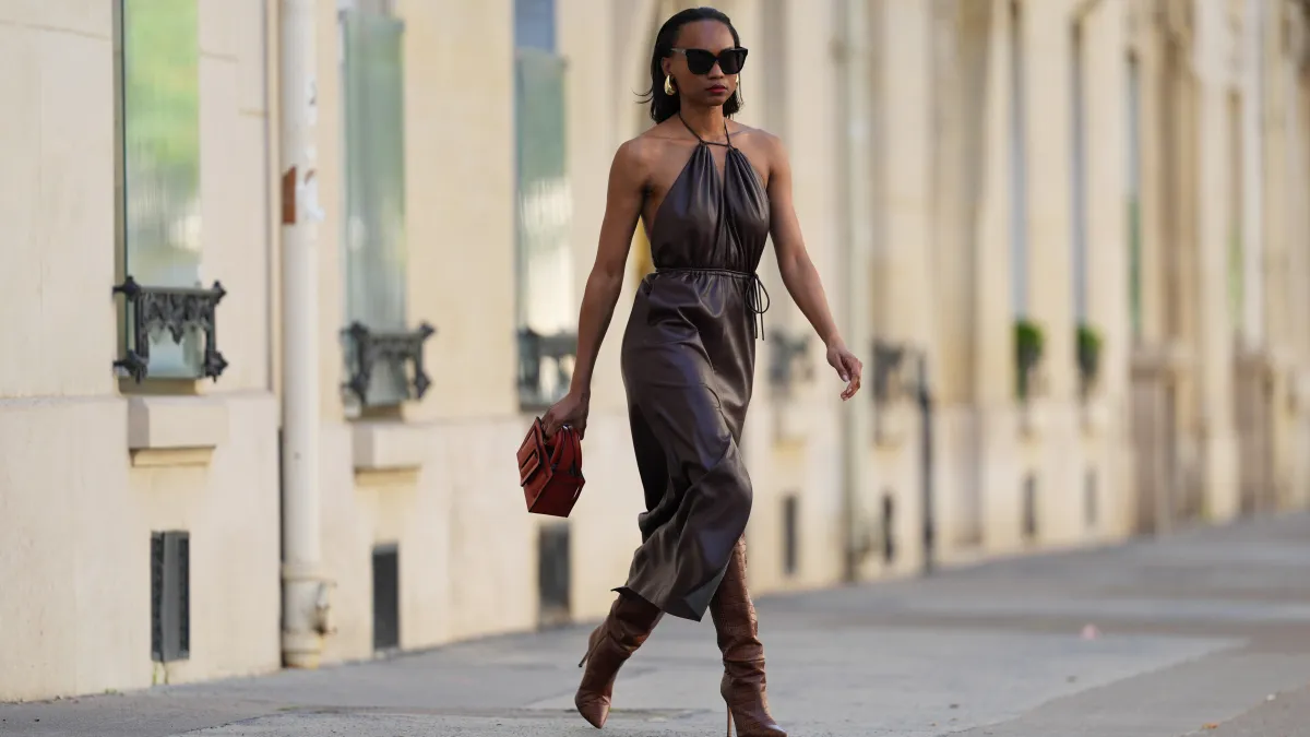 PARIS, FRANCE - APRIL 13: Emilie Joseph wears sunglasses, golden earrings, a brown leather gathered sleeveless dress, a red leather bag, brown leather boots / pointed shoes high heels with crocodile patterns, during a street style fashion photo session, on April 13, 2024 in Paris, France. (Photo by Edward Berthelot/Getty Images)