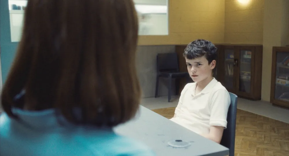 A boy looks at an adult woman in Adolescence.