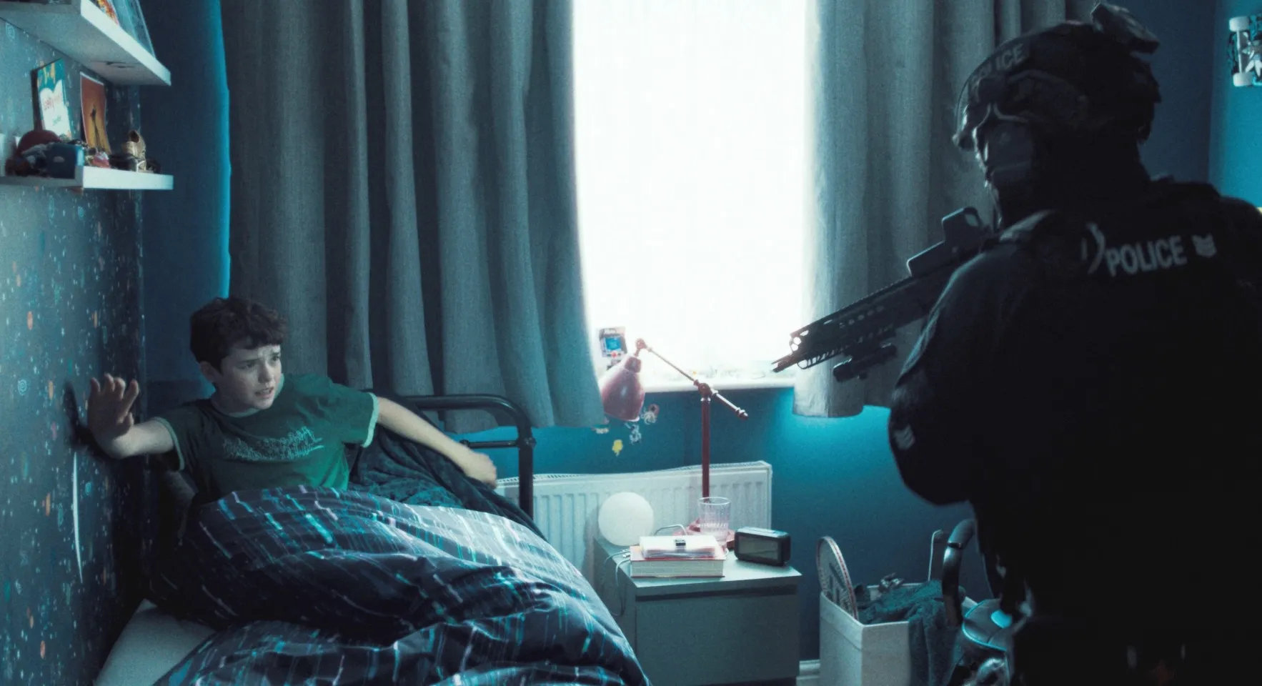 A cop aims a gun at a kid in his bed in Adolescence.