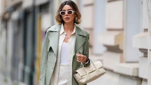 PARIS, FRANCE - APRIL 07: Katie Giorgadze wears sunglasses from Celine, golden earrings, a sage pastel green smooth leather trench coat from Mackage, a cream colored mini skirt, a white tank top from Uniqlo, a beige oversize rhinestone sparkly leather shirt from Frame, a cream color / white leather bag from Tod's, during a street style fashion photo session, on April 07, 2024 in Paris, France.