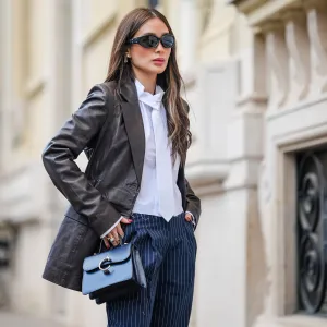 PARIS, FRANCE - APRIL 23: Heart Evangelista wears sunglasses from Gentle Monster x Margiela, earrings, a black leather jacket from Rotate, a white shirt from The Frankie Shop, a white tie, blue striped pants from The Frankie Shop, a blue leather bag from Cartier, during a street style fashion photo session, on April 23, 2024 in Paris, France.