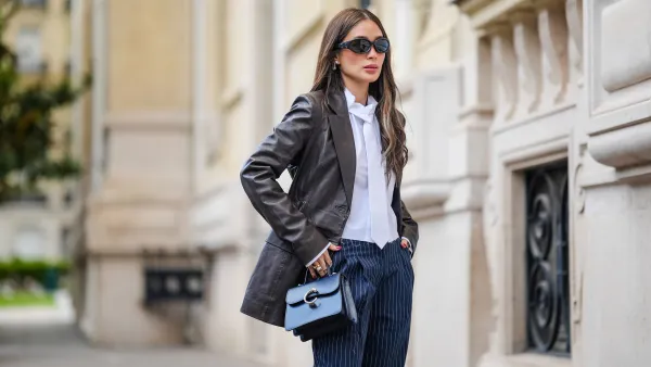 PARIS, FRANCE - APRIL 23: Heart Evangelista wears sunglasses from Gentle Monster x Margiela, earrings, a black leather jacket from Rotate, a white shirt from The Frankie Shop, a white tie, blue striped pants from The Frankie Shop, a blue leather bag from Cartier, during a street style fashion photo session, on April 23, 2024 in Paris, France.