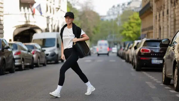 PARIS, FRANCE - APRIL 21: Diane Batoukina wears a black with embroidered NY logo pattern cap from New Era, a white with black faded logo print pattern t-shirt from Saint Laurent Paris, a black wool pullover knot at the shoulder, a black shiny leather large shoulder bag from Zadig&Voltaire, black legging pants, white socks, white leather and suede sneakers from Chanel, during a street style fashion photo session, on April 21, 2023 in Paris, France.
