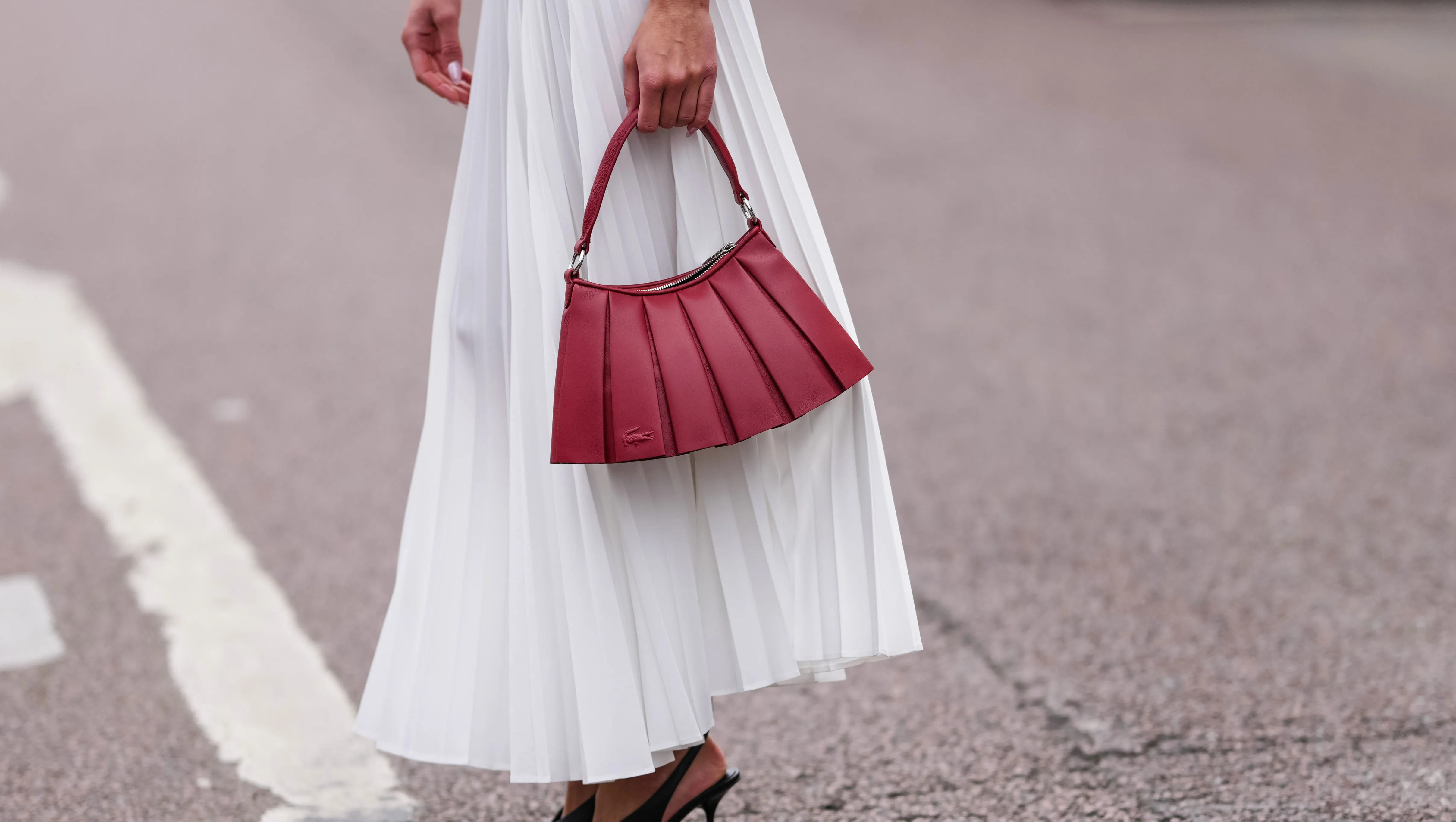 PARIS, FRANCE - MARCH 09: Amalie Bladt wears white pleated Lacoste midi skirt, a gold bracelet, a gold watch, shiny dark red Lacoste leather bag, outside Lacoste, during the Paris Fashion week Women's Fall/Winter 2025-2026 on March 9, 2025 in Paris, France. (Photo by Edward Berthelot/Getty Images)