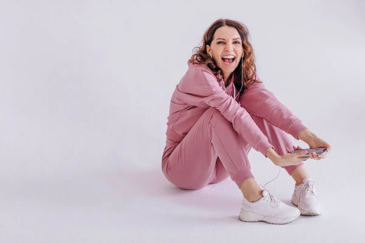 Brunette woman wearing pink track suit and listening to music, holding smartphone