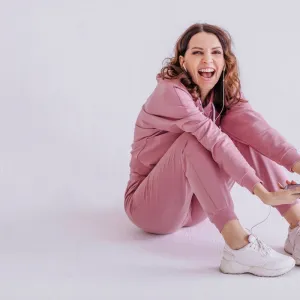 Brunette woman wearing pink track suit and listening to music, holding smartphone