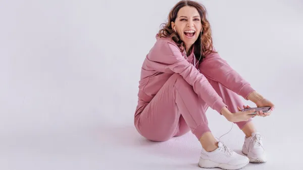 Brunette woman wearing pink track suit and listening to music, holding smartphone