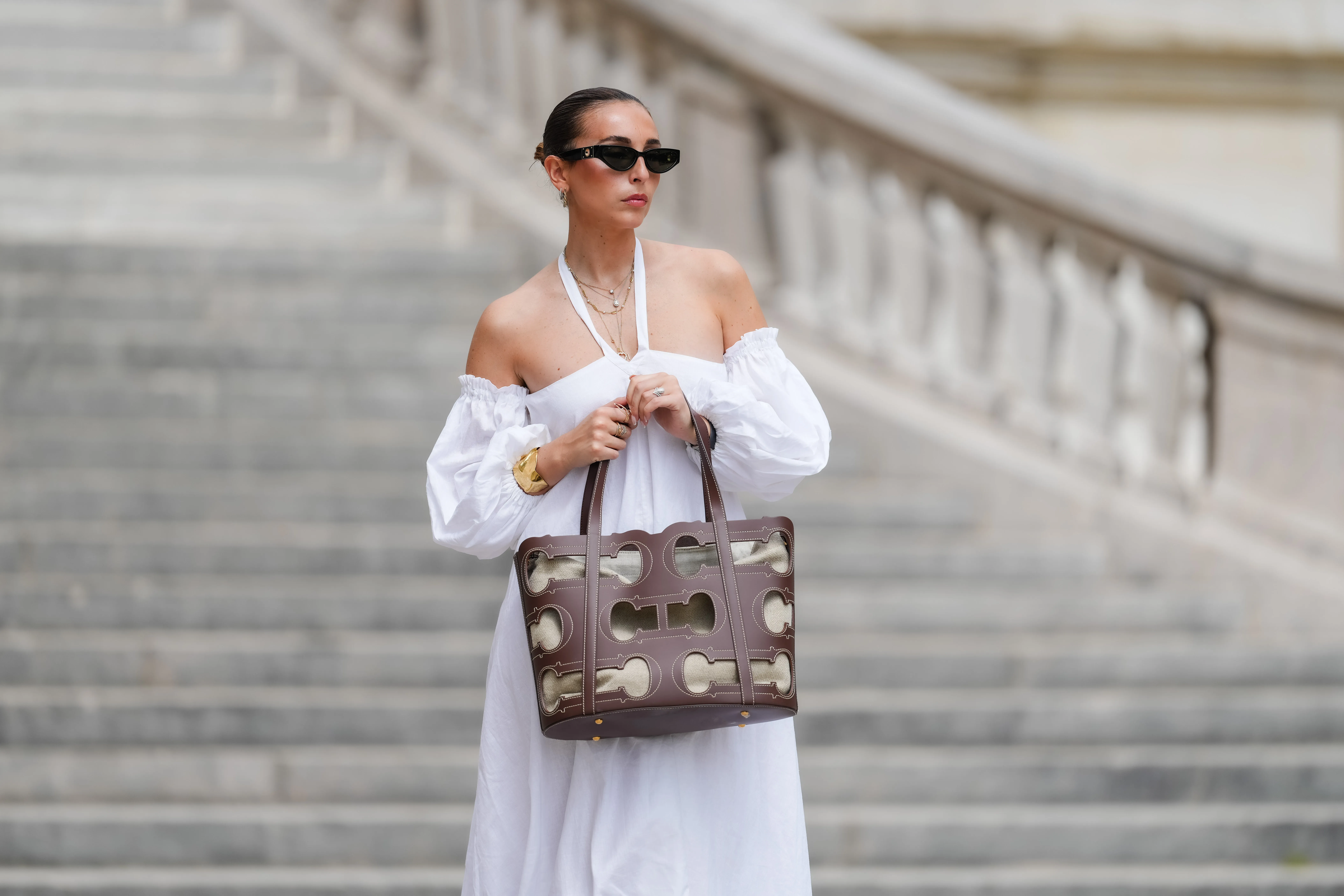 Gabriella Berdugo wears sunglasses, earrings, a white off-shoulder linen gathered dress from kalita with balloons / puff sleeves, a brown summer bag from Carolina Herrera in brown leather, during a street style fashion photo session, on May 12, 2024 in Paris, France.