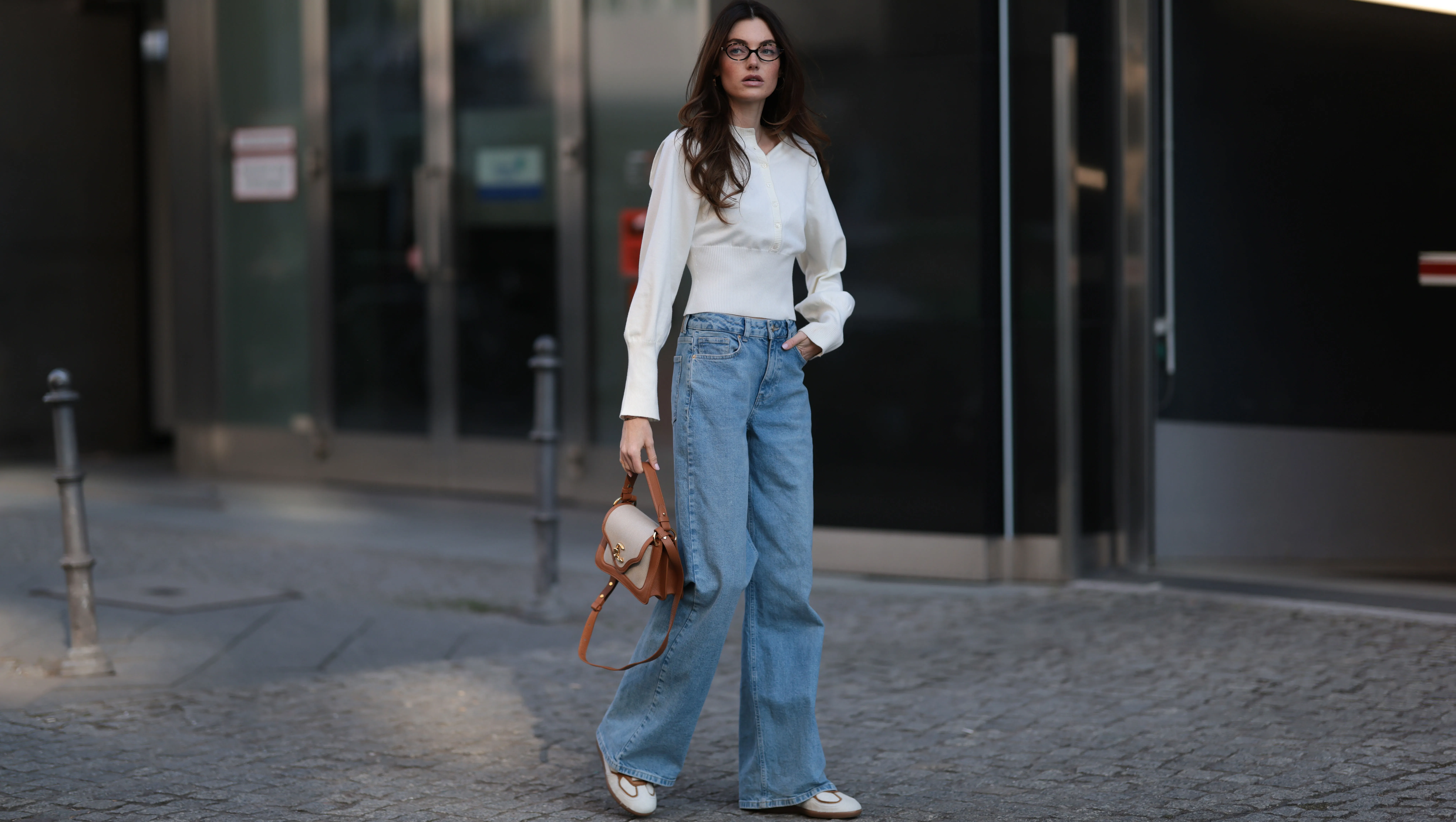BERLIN, GERMANY - MARCH 21: Celine Bethmann seen wearing Miu Miu brown oval framed statement glasses, Cie Cie fitted ivory long-sleeve cotton henley top with a structured waist detail, Cie Cie high-waisted, light-wash wide-leg jeans that add a relaxed yet sophisticated touch, Cochinelle two-tone leather handbag in beige and brown, adding an elegant contrast and Alohas classic soft cream suede and light brown leather sneakers with a vintage-inspired silhouette, on March 21, 2025 in Berlin, Germany. (Photo by Jeremy Moeller/Getty Images)