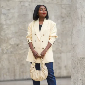 PARIS, FRANCE - JUNE 29: Carrole Sagba @linaose wears a beige oversized blazer jacket, a black top, blue denim jeans pants, a beige leather bag, a golden ring, yellow platform shoes, on June 29, 2021 in Paris, France. (Photo by Edward Berthelot/Getty Images)
