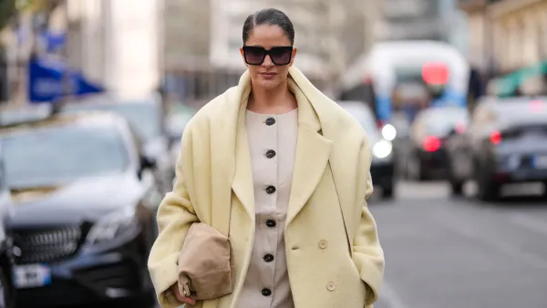 PARIS, FRANCE - MARCH 09: Gili Biegun wears black sunglasses, cream buttoned blazer jacket, light yellow oversized double breasted wool coat, dark yellow scarf, light brown suede bag, outside Akris, during the Paris Fashion week Women's Fall/Winter 2025-2026 on March 9, 2025 in Paris, France. (Photo by Edward Berthelot/Getty Images)