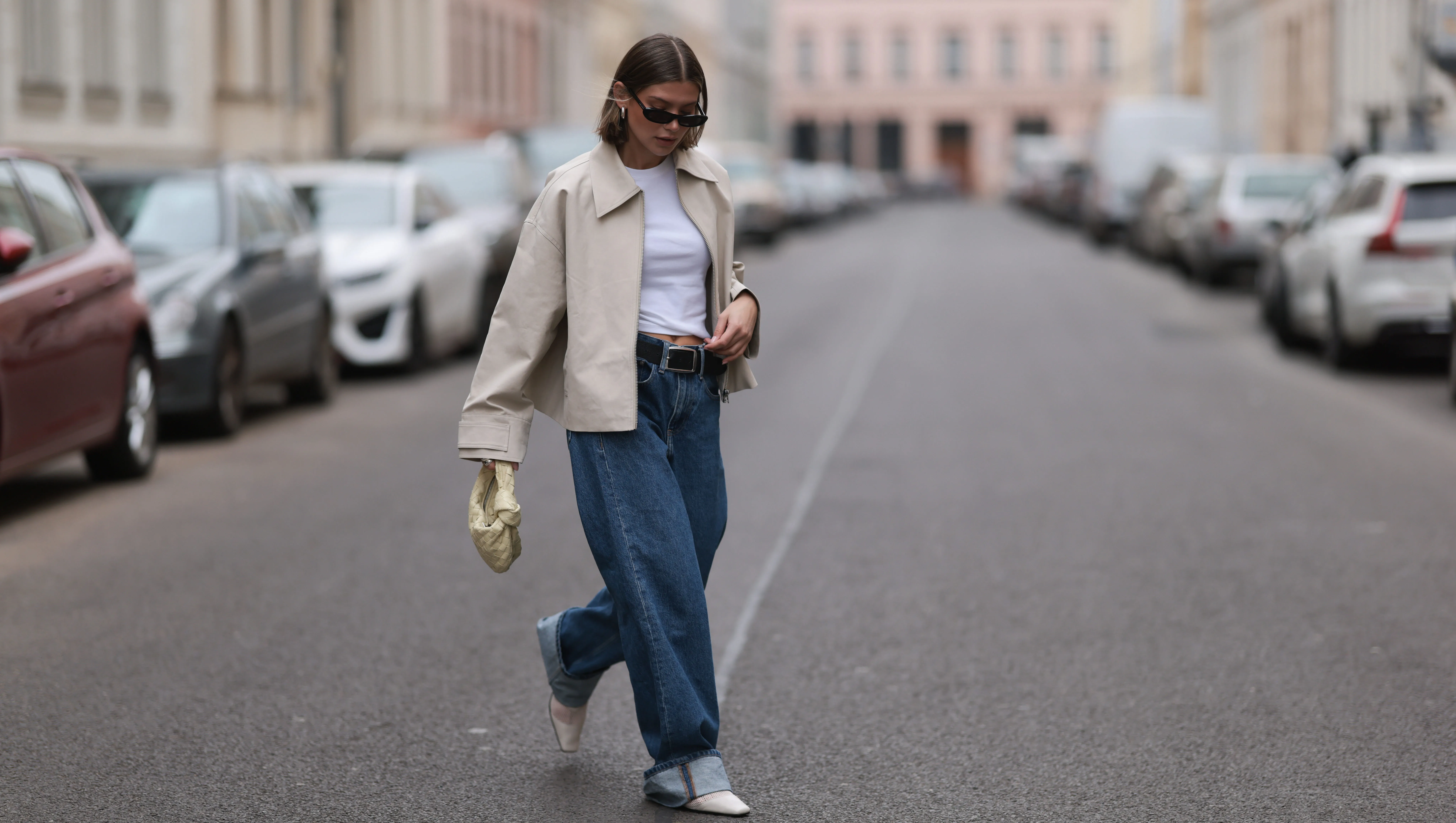 BERLIN, GERMANY - APRIL 12: Sophia Geiss seen wearing Saint Lauren black sunglasses, Uniqlo white cotton basic top, Calvin Klein blue denim baggy wide leg jeans pants, black leather belt, Meotine creamy white canvas jacket, Bottega Veneta creamy white / vanilla leather mini Jodie bag and Vagabond white leather mesh ballerinas, on April 12, 2024 in Berlin, Germany.