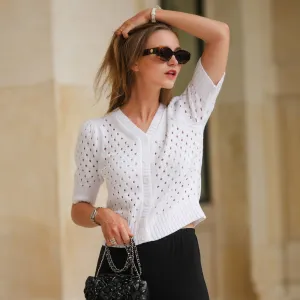 PARIS, FRANCE - MAY 12: Segolene Hyppolite wears sunglasses, a white wool cardigan / top from Agnes B, a white flower shaped bracelet, a Chanel bag with floral texture / details, black pants from Agnes B, during a street style fashion photo session, on May 12, 2024 in Paris, France. (Photo by Edward Berthelot/Getty Images)