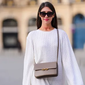 PARIS, FRANCE - APRIL 17: Bianca Derhy wears black sunglasses from Celine, gold and rhinestones earrings, gold chain necklaces, a white embossed braided wool pattern oversized long sleeves / midi dress, a gray brown matte leather crossbody bag with gold chain buckle, a gold ring, during a street style fashion photo session, on April 17, 2022 in Paris, France. (Photo by Edward Berthelot/Getty Images)