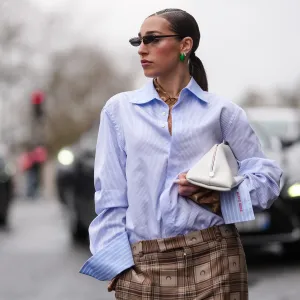 PARIS, FRANCE - MARCH 10: Ginevra Mavilla wears black sunglasses, dark green earrings, dark brown Marine Serre monogram Marine Serre buttoned up long sleeve shirt, light blue navy blue striped half buttoned long sleeve Marine Serre shirt, white clutch leather bag, outside Marine Serre, during the Paris Fashion week Women's Fall/Winter 2025-2026 on March 10, 2025 in Paris, France. (Photo by Edward Berthelot/Getty Images)