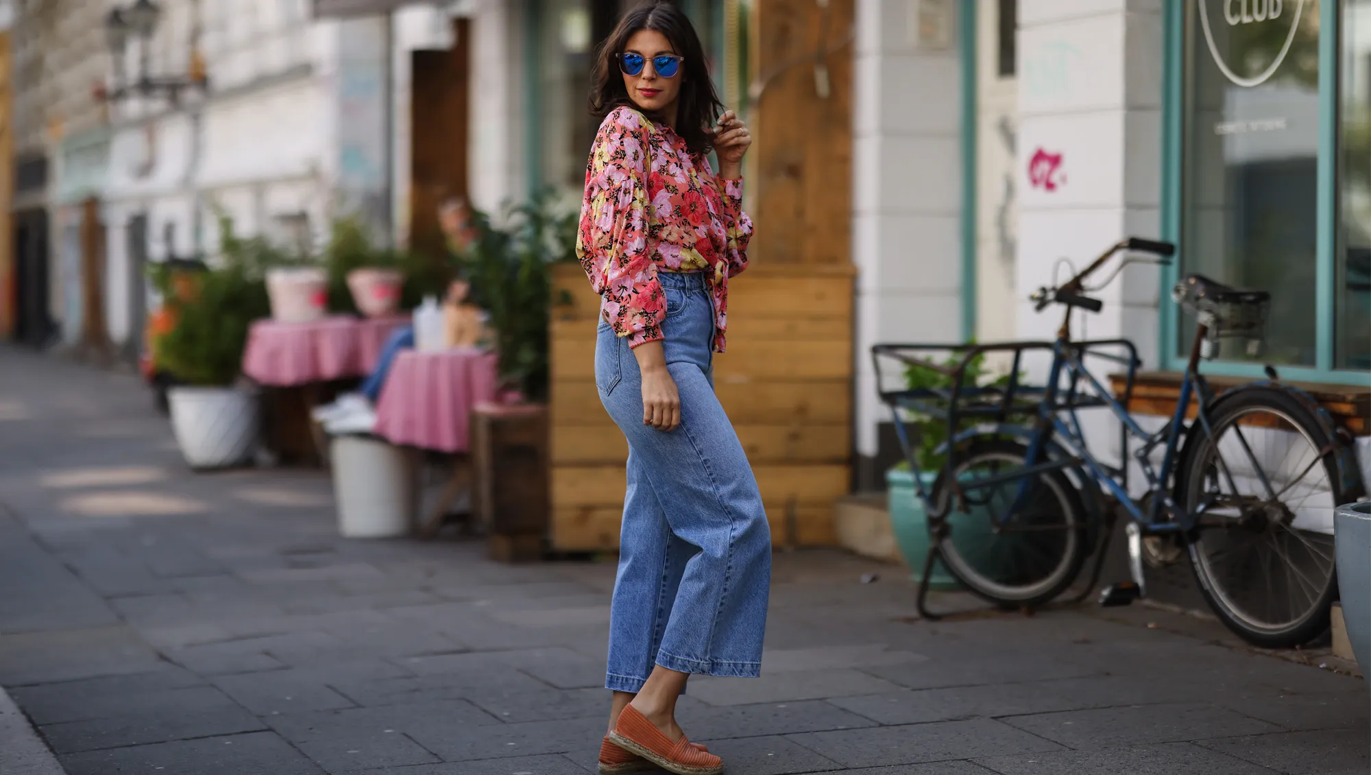 Anna Wolfers wearing colorful floral blouse, sunglasses, blue jeans and orange espadrilles on May 01, 2021 in Hamburg, Germany.
