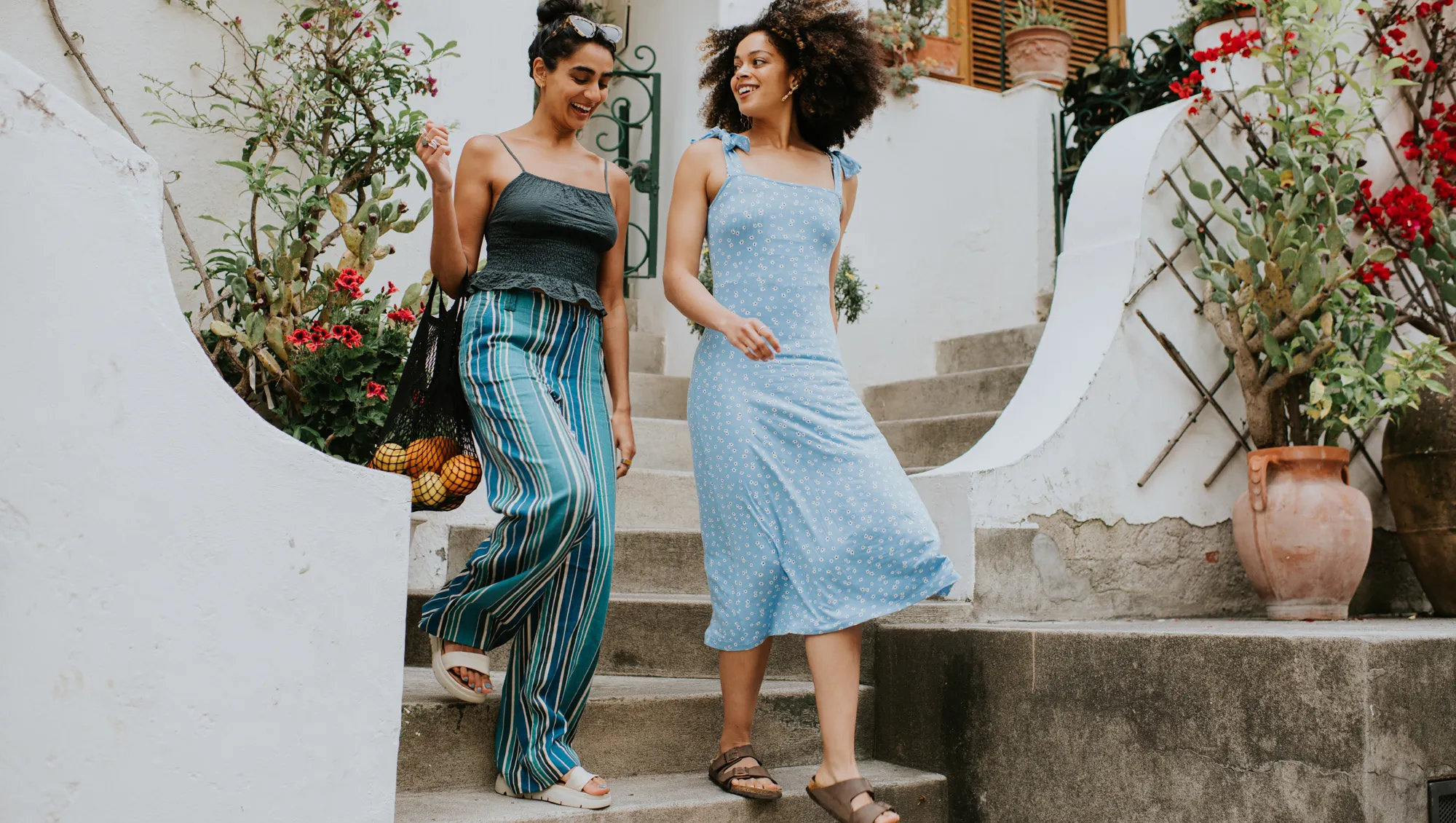 Two beautiful young woman descend a set of concrete steps from European-style apartments as they have a conversation.