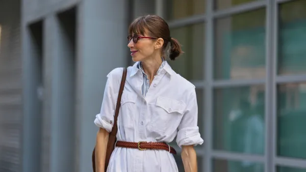NEW YORK, NEW YORK - SEPTEMBER 15: A guest wears their hair pulled back into a low ponytail with straight bangs, small round burgundy sunglasses with dark lenses, a silver metal watch with a black face on the left wrist, a brown leather shoulder bag with a thin strap, a white button-front jumpsuit in a lightweight woven fabric with chest flap pockets and rolled sleeves, a blue-and-white striped shirt collar peeking at the neckline, a braided brown leather belt with a gold-toned buckle cinching the waist, outside Zankov, during New York Fashion Week, on September 15, 2025 in New York, New York (Photo by Edward Berthelot/Getty Images)