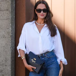 COPENHAGEN, DENMARK - AUGUST 6: Gabrielle Caunesil Pozzoli wears black sunglasses, white beaded necklace, white button up long sleeve rolled up shirt, black leather bag, gold and black belt, gold rings, light blue denim jean pants, outside Remain, during the Copenhagen Fashion Week Spring/Summer 2024-2025 on August 6, 2024 in Copenhagen, Denmark. (Photo by Edward Berthelot/Getty Images)