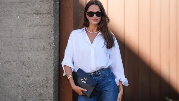 COPENHAGEN, DENMARK - AUGUST 6: Gabrielle Caunesil Pozzoli wears black sunglasses, white beaded necklace, white button up long sleeve rolled up shirt, black leather bag, gold and black belt, gold rings, light blue denim jean pants, outside Remain, during the Copenhagen Fashion Week Spring/Summer 2024-2025 on August 6, 2024 in Copenhagen, Denmark. (Photo by Edward Berthelot/Getty Images)