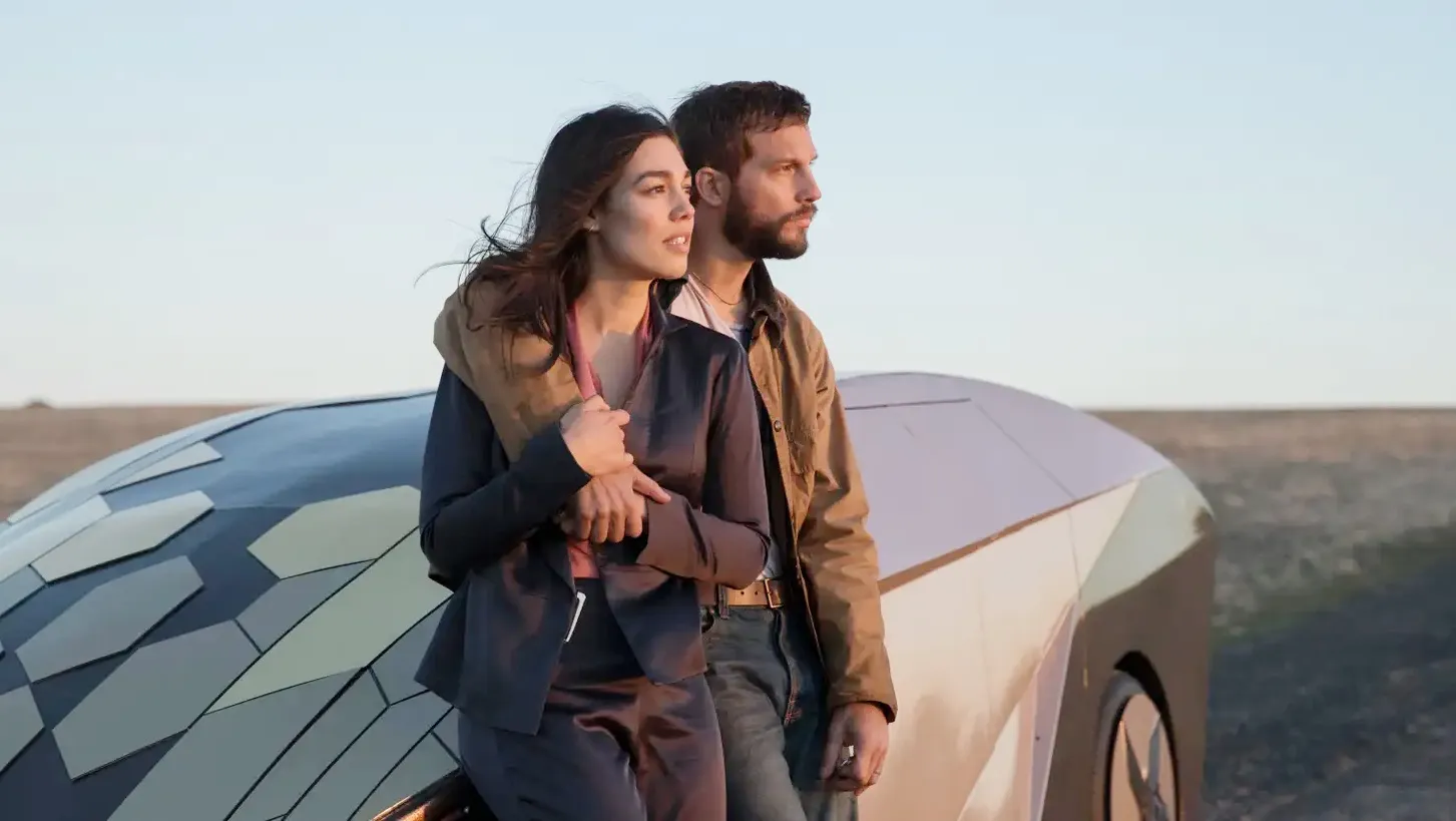A man and a woman lean on a car outside in Upgrade.
